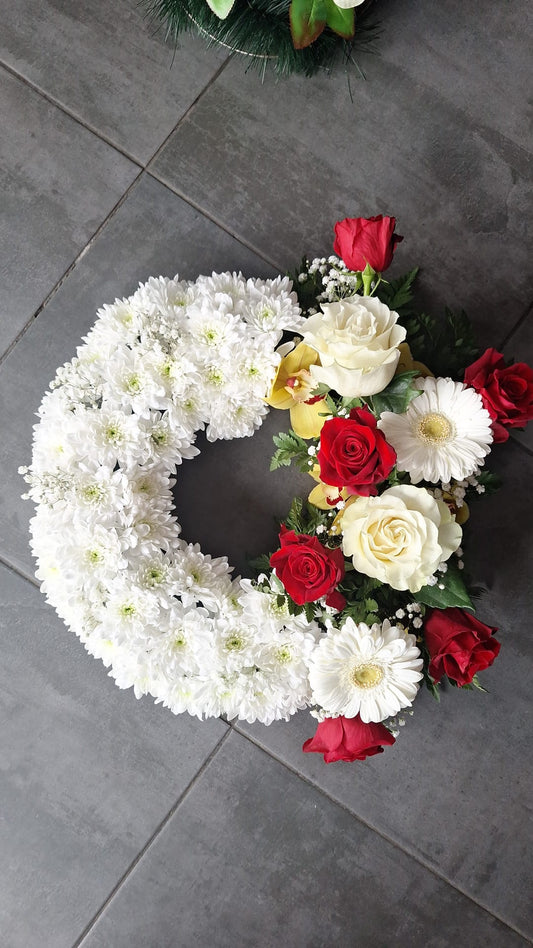 Coroana funerara rotunda, cu baza alba din crizanteme, accente de trandafiri albi, gerbera si orhidee